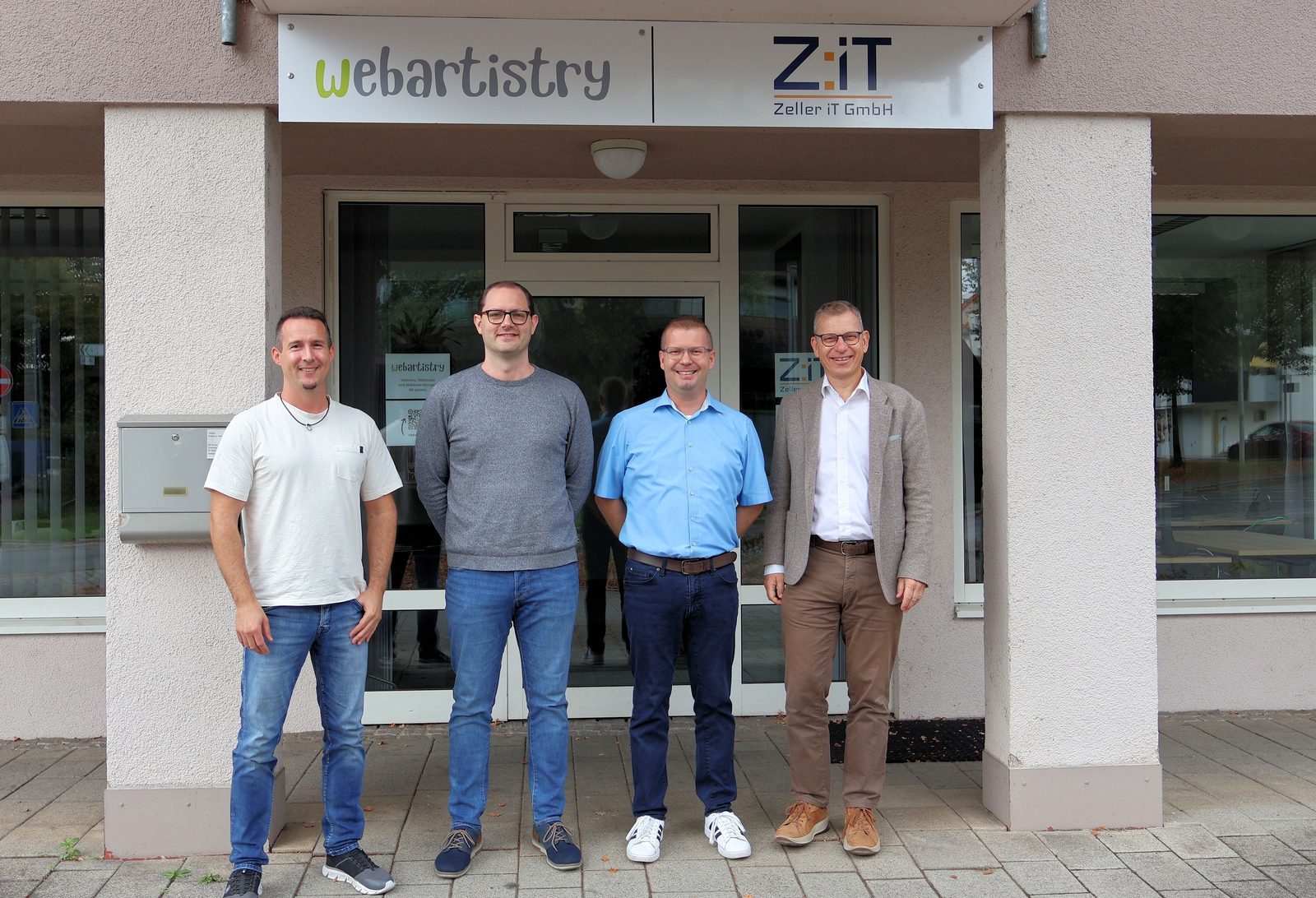 	Vier Männer stehen vor dem Eingang eines Bürogebäudes, darüber die Schilder von webartistry und Zeller iT GmbH: Florian De Felice, Sebastian Radon, Christopher Zeller und Bürgermeister Steffen Weigel.